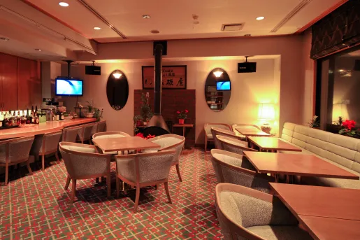 Bar and lounge with square dining tables and cushioned chairs, with a fireplace in the back