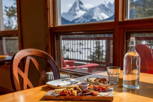 Dining table with a wooden plank with food, and a glass bottle of water to the right