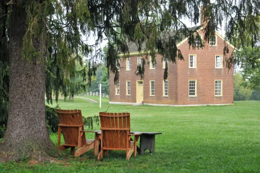 Two wooden chairs on a grass field, with a brick building in the background