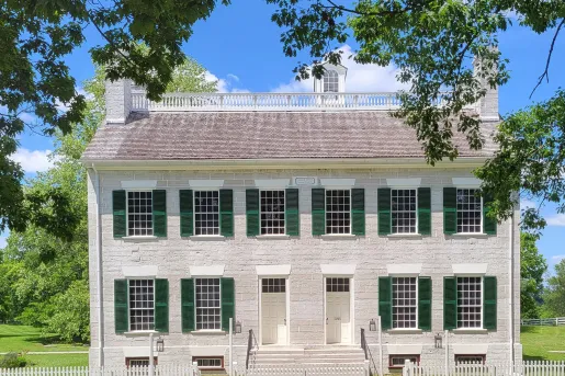 White brick building with large grass field and tall trees in the background