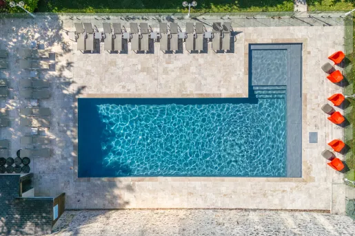 Sky view of an outdoor pool, surrounded by reclining chairs and grass fields