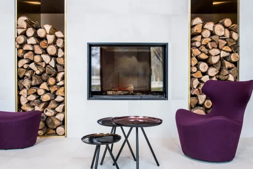 Seating area with purple, cushioned chairs, black circular tables and a fireplace in the background