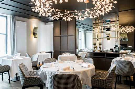 Hotel dining area with checkered chairs and circular white tables, with large light fixtures above