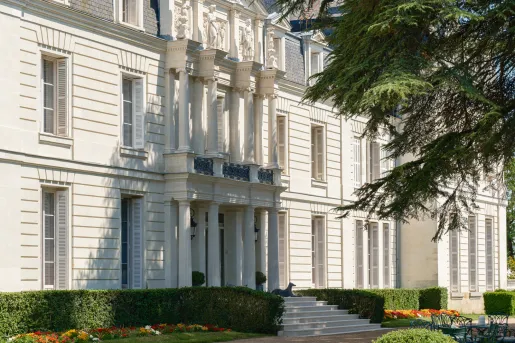 Exterior view of a white, stone building with large pillars and trimmed bushes