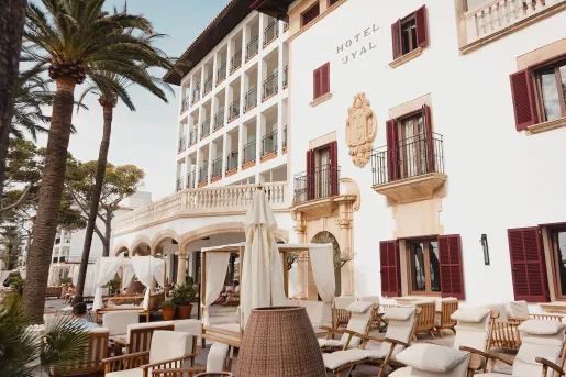 Exterior view of white hotel with large balconies and reclining chairs outside