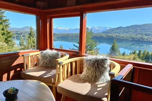 Two chairs with fuzzy pillows next to a large window, overlooking a lake