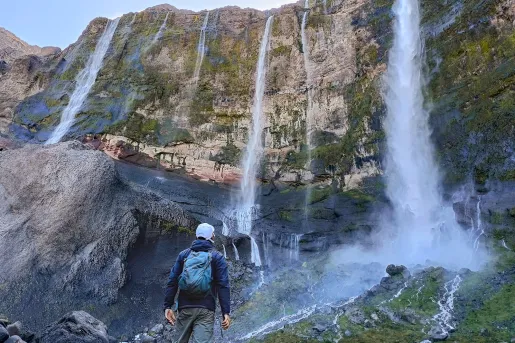 Hiker looking up at a tall cliff with multiple, active waterfalls