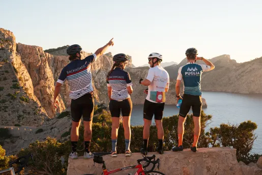 Group of people wearing biking gear, standing on a ledge looking out to a lake