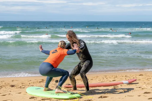Man and woman practicing surfing on the sand in front of the ocean