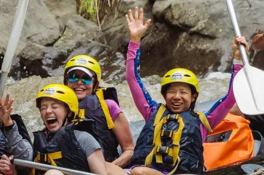 Group of people on a gray raft, paddling on a river
