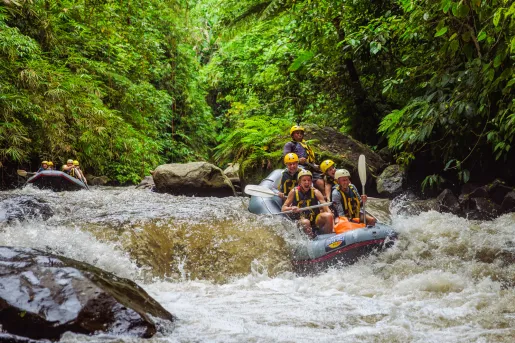 Group of people smiling while paddling on a raft through a river