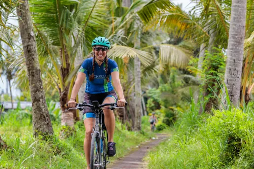 Woman smiling while riding a bike through a road surrounded by palm trees