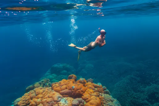 Man diving in the ocean with large coral reefs under