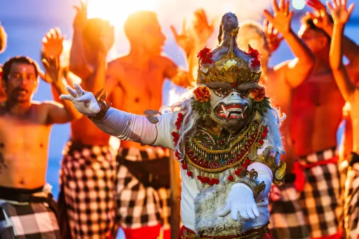 Person in traditional attire dancing, while a group of men behind them are dancing