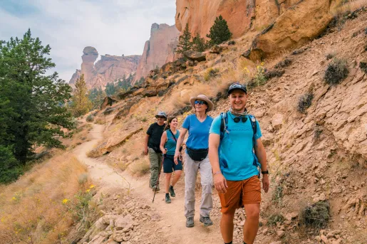 Group of men and women hiking on a dirt trail with large mountains in the background