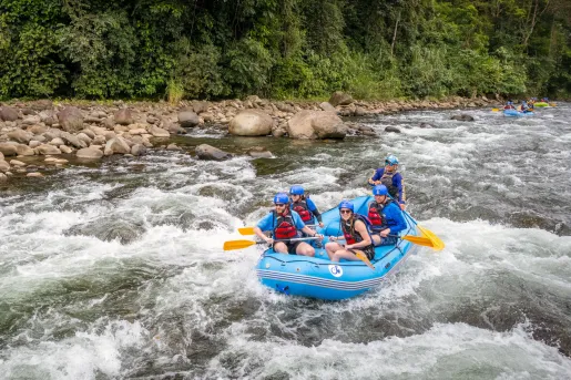 Group of people paddling in a blue raft in an active river