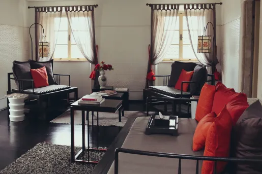 Three wooden chairs with pillows and cushions in a room with black floors and long curtains on the windows