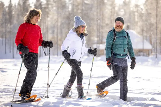 Women and two men with hiking poles and snow shoes, walking in a valley of snow