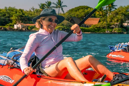 Woman wearing a hat and sunglasses, paddling on an orange kayak