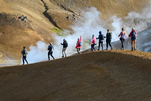 Group of people walking along a dirt trail on a hill, with fog in the background