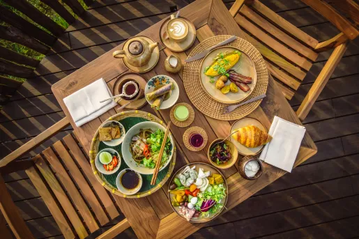 Top-down view of restaurant table full of plates of colorful food and two wooden chairs