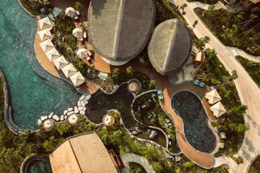 Top-down view of an outdoor pool and gray villas, with sandy paths along the sides