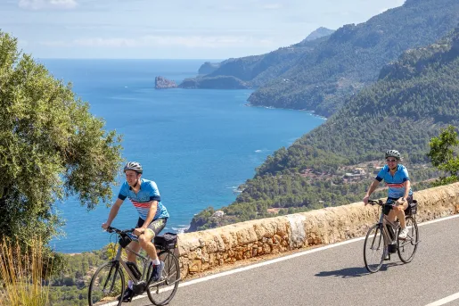 Two people riding their bikes on a road, with the ocean in the distance