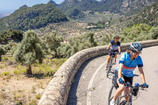 Two women riding a bike on a road with a large grass and tree valley in the background