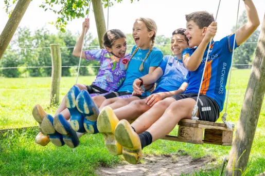 Group of kids smiling and laughing, while sitting and swinging on a wooden swing