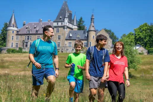 Family smiling while walking through a grassy field, with a castle-like building in the background