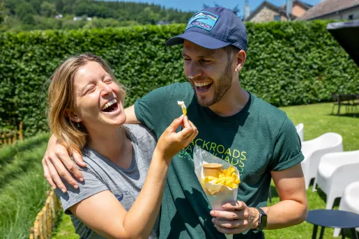 Man and woman smiling with their arms around their shoulders, holding a cone of fried potatoes