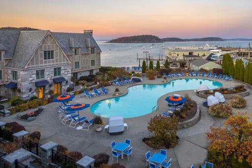 Outdoor pool, surrounded by blue reclining chairs and the ocean in the background