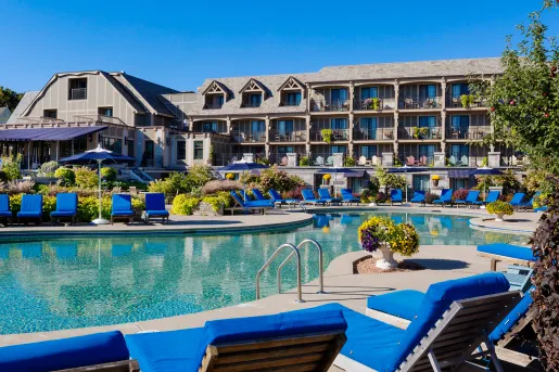 Outdoor pool surrounded by blue reclining chairs, and a hotel building in the background