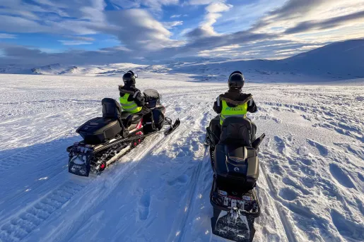Two people riding on snow mobiles in a vast valley of snow