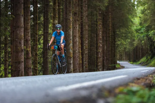 Woman riding a bike on a road, surrounded by a forest