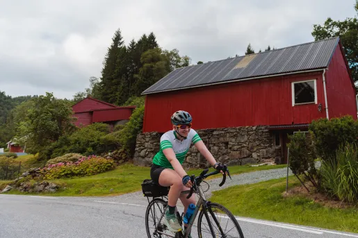 Person smiling while riding a bike in front of a red house