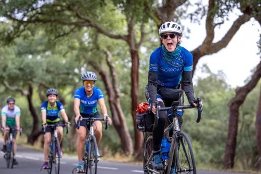 Group of people riding bikes on an empty road, surrounded by tall trees