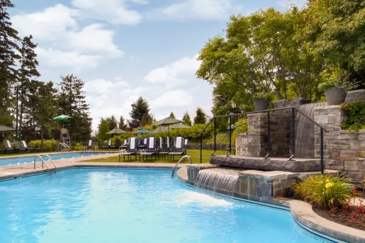 Outdoor pool with a small fountain to the right, and chairs in the background