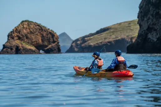 Two people on an orange and yellow kayak, paddling in the middle of the ocean