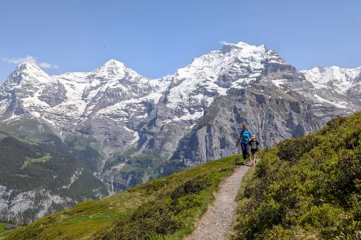 Mom and son hiking on a gravel trail with snow-capped mountains in the background