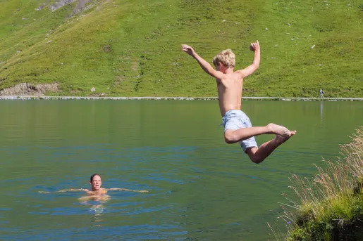 Boy jumping into a lake with his dad swimming in the water