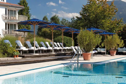 Outdoor pool with white pool chairs and blue umbrellas