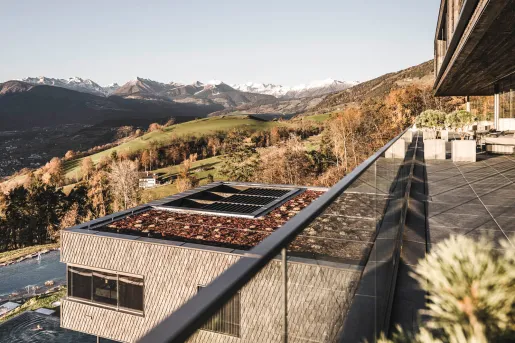 Outdoor balcony with a glass barricade, overlooking a large grassy valley and mountains