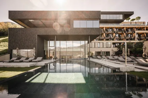Outdoor pool surrounded by gray chairs, and a black and beige building with large windows in the back