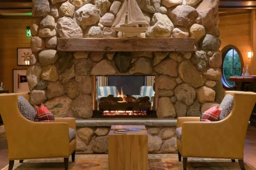 Indoor lodge-style room with a stone fireplace and two leather chairs in front