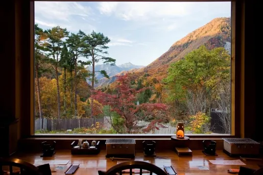 Desk in front of a large window, overlooking orange and green trees on a hill