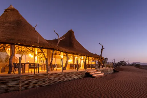 Exterior view of two large huts with the sand of a desert in front