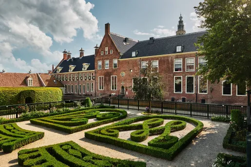 Exterior view of brick hotel building with a garden and trimmed hedges in the back