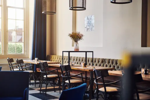 Cafe with cushioned sofas and black chairs around square tables