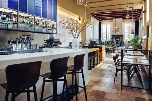 Bar with white counter top, wooden stools and tables and chairs in the back